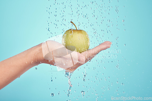 Image of Water splash, cleaning and hands with apple in studio isolated on a blue background. Nutritionist, fruits and model or woman washing food for healthy diet, vitamin c or skincare, beauty or wellness.