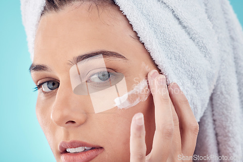 Image of Towel, face and woman with skincare cream in studio isolated on a blue background. Portrait, dermatology and young female model apply lotion cosmetics, creme or facial moisturizer for healthy skin.