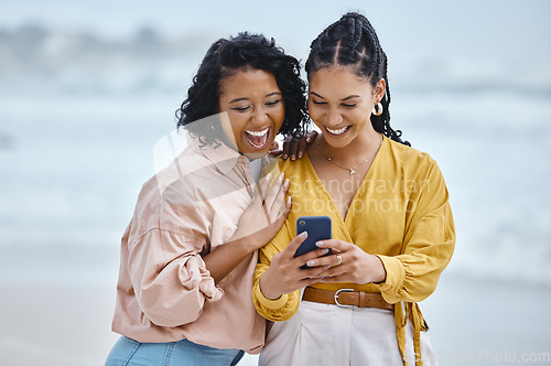 Image of Phone, beach and meme with black woman friends laughing together by the ocean or sea in the morning. Nature, joke or social media with a young female and friend reading a funny text on the coast