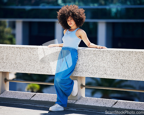 Image of Portrait, fashion and serious with a black woman in the city on a bridge, looking relaxed during summer. Street, style or urban and an attractive young female posing outside with an afro hairstyle