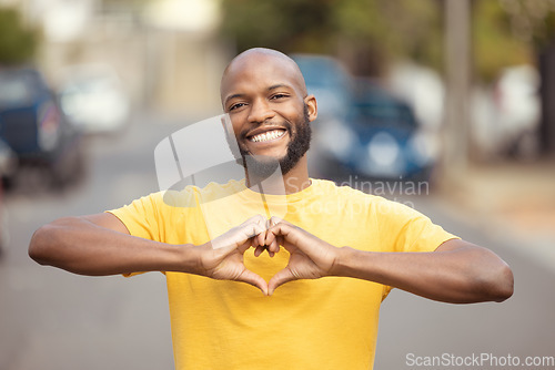 Image of Portrait, man and hand, heart and love in a city, happy and smile against blurred background space. Emoji, hands and face of male relax with finger, frame and loving message, gesture and travel sign