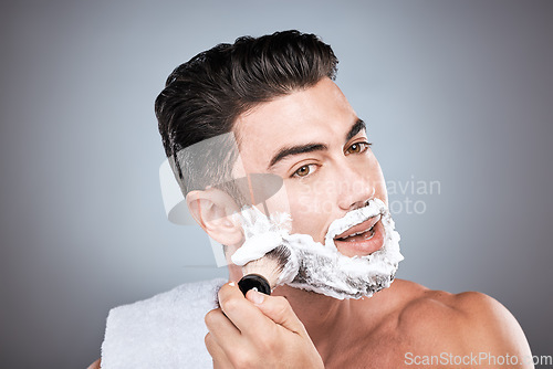 Image of Shaving cream, face and man with brush in studio isolated on a gray background for hair removal. Beard care portrait, grooming and male model with facial product, foam or gel to shave for wellness.