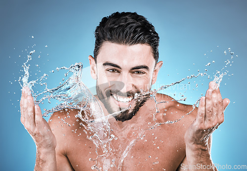 Image of Portrait, water splash and a man model washing his face in studio on a blue background for hygiene or hydration. Bathroom, skincare and cleaning with a handsome male splashing his skin for beauty