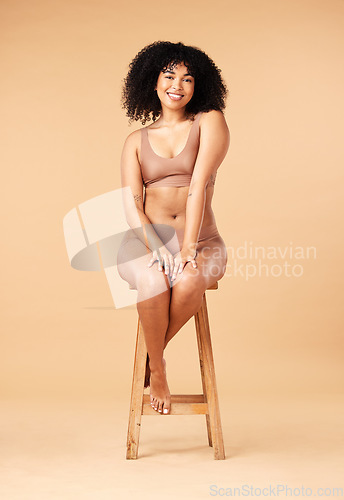 Image of Body positive, beauty and black woman sitting on a chair for skincare and self care isolated in a studio brown background. Plus size, portrait and natural model smile, happy and glow due to cosmetic