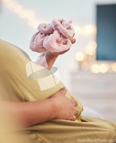 Image of Baby shoes, pregnant stomach and woman hands with baby clothes holding her abdomen. Mother, mom love and gratitude of a new mama with family care for pregnancy in a living room lounge with slippers