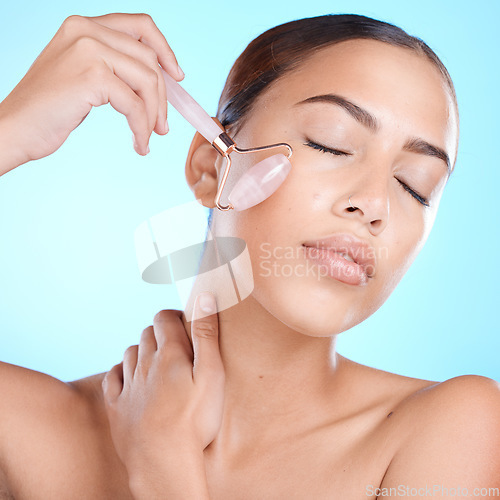 Image of Skincare, rose quartz and face massage in studio for beauty, anti aging and skin wellness on blue background. Facial, derma roller and girl model relax with luxury, skin and product while isolated