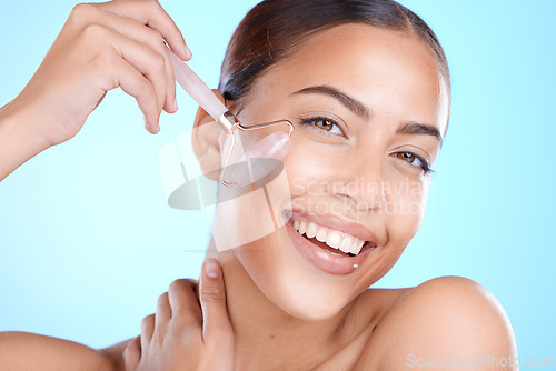 Image of Skincare, portrait and woman with face roller in studio for beauty, wellness and anti aging treatment on blue background, Facial, massage and girl model relax with rose quartz for lymphatic drainage