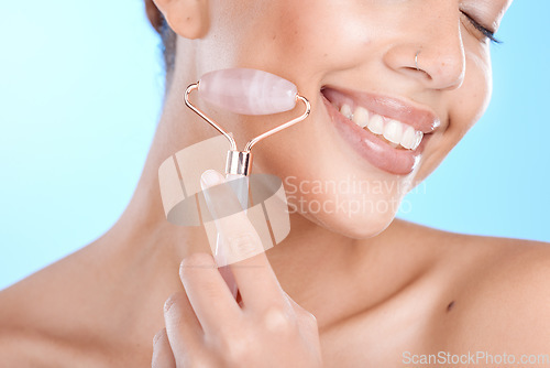 Image of Skincare, massage and woman with face roller in studio for beauty, wellness and anti aging treatment on blue background, Facial, happy and girl model relax with rose quartz product and isolated