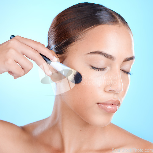 Image of Makeup brush, cosmetics tool and woman face with makeup and blush in a studio. Blue background, isolated and young person with eyes closed feeling calm from skincare and beauty with self care