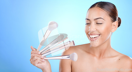 Image of Woman, brushes and smile for makeup, cosmetics or beauty against a blue studio background. Female gen z model smiling for cosmetic skincare, facial glow aesthetic or foundation product on mockup