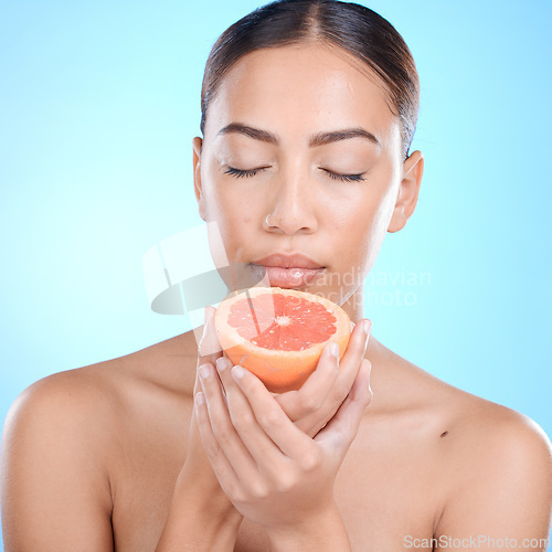 Image of Skincare, woman and grapefruit scent for in studio for beauty, smell and cosmetics on blue background. Fruit, citrus and product for girl skin model relax in luxury, pamper or routine while isolated