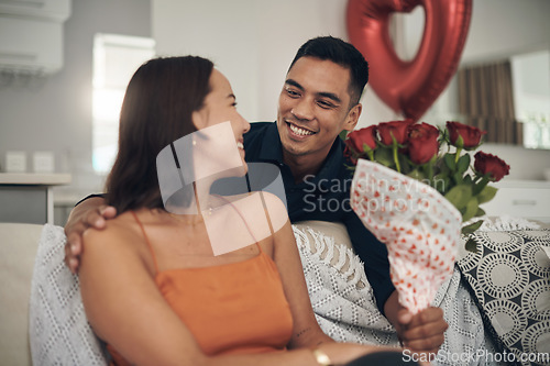 Image of Valentines day, flowers and couple on a living room sofa with a present and a smile. Happy, love and care of young people together with celebration rose on a date in a house on a couch with a gift