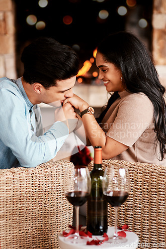 Image of Young couple on a date, romantic restaurant evening and kiss on the hand at cafe fireplace with wine glasses. Happy people in love, valentines day together and girlfriend smile at handsome boyfriend