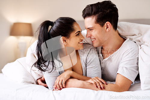 Image of Happy, love and interracial couple in bed together in home holding hands at night. Smile, morning and marriage of an Indian woman and man with care and relax happiness in a bedroom in a house