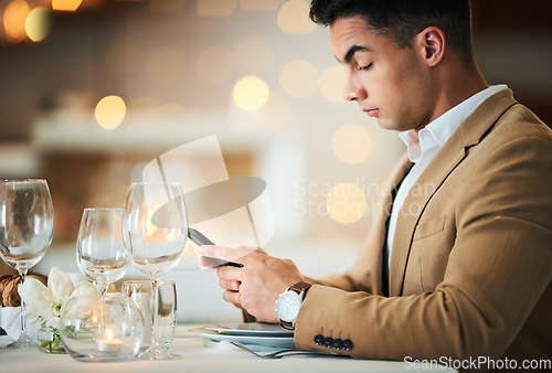 Image of Man, texting and phone at restaurant table for food, night and waiting for valentines day date. Young male, smartphone and wine glass for fine dining, bottle service or drink at dinner celebration