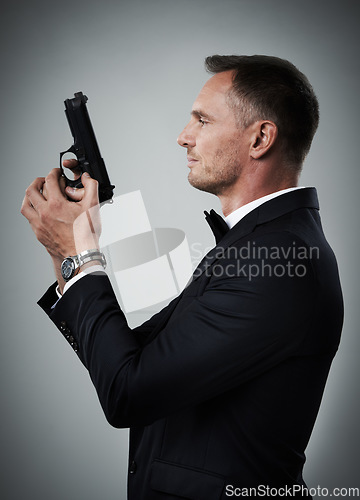 Image of Agent man, profile and gun with suit for mission, justice or espionage by grey studio background. Government spy, detective and firearm with designer tuxedo, secret information and undercover work