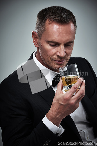 Image of Man, tuxedo fashion and whiskey in studio isolated on a gray background. Alcohol, whisky and mature male model in stylish, designer and classy suit smelling aroma of alcoholic beverage in glass.