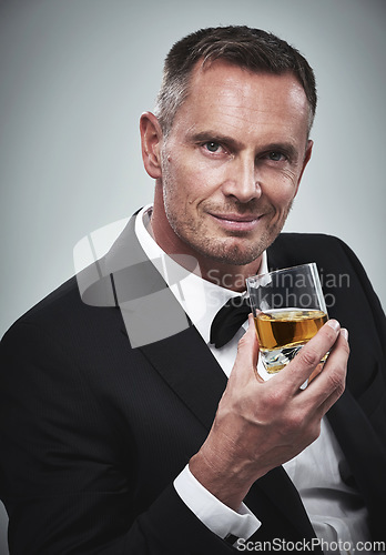 Image of Portrait, man and a glass of whisky for celebration, smile and guy on grey studio background. Face, male and gentleman in a suit, alcohol beverage or drinking for achievement, confidence or happiness