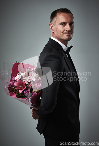 Image of Surprise, portrait and man with flowers for a date isolated on a grey studio background. Classy, gift and mature person in a suit with a bouquet of roses as a present for valentines day on a backdrop