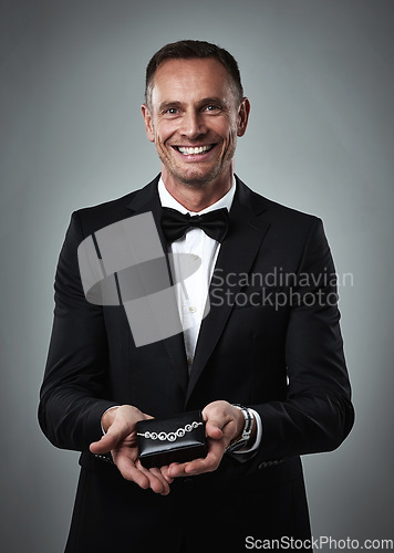 Image of Jewelry, smile and portrait of a man giving a valentines present in a studio. Isolated, gray background and happy person in a suit with happiness holding a necklace gift feeling love and classy