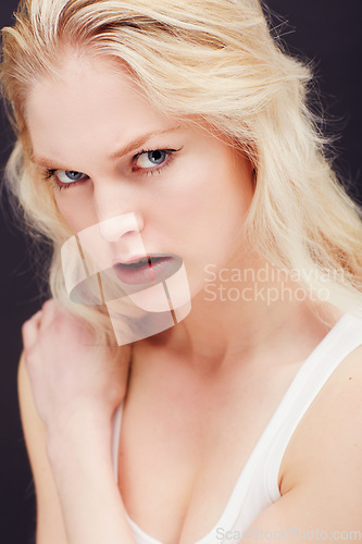 Image of Portrait, beauty or fierce and a model woman in studio on a dark background frowning with confidence. Face, frown and skincare with an attractive young blonde female posing indoor for desire