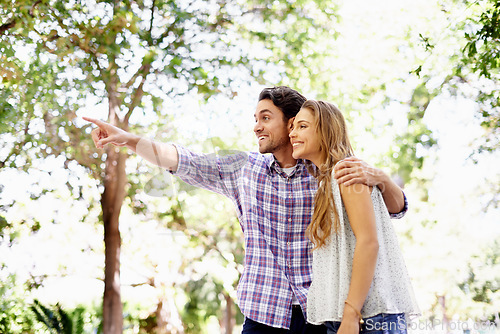 Image of Couple, park and date of a woman and man together with love, care and hug in nature. Green trees, sunshine and happy people outdoor excited by pointing in the sun with happiness and good mood