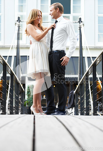 Image of Romance, embrace and couple on a date in the city with love, happiness and classy in France. Happy, celebration and woman helping a man with a tie while on a bridge during valentines day in town