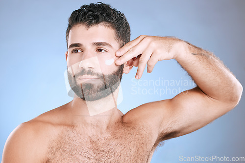 Image of Face, cream and man serious for skincare, sunscreen product and clean wellness on blue background. Male model, facial lotion and body cosmetics for natural beauty, studio aesthetics or self care glow