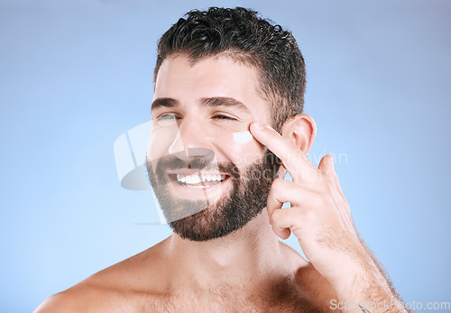 Image of Face, cream and man laughing for beauty, sunscreen product and clean wellness on blue background. Happy male model, facial lotion and body cosmetics for natural skincare, studio aesthetics and smile