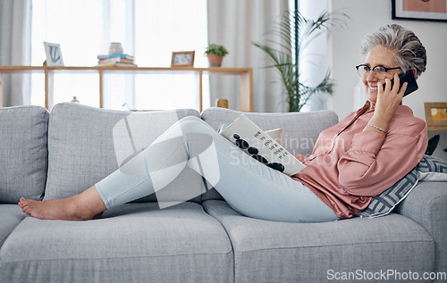 Image of Phone call, reading and relax on the sofa with a senior woman in the living room of her home over the weekend. Mobile, books and retirement with a mature female sitting on a couch in the lounge