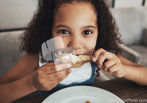 Image of Lunch, portrait and child eating chicken in the dining room at a party, dinner or event at home. Hungry, happy and girl kid enjoying food or meal at the table for snack, hunger or craving at a house.