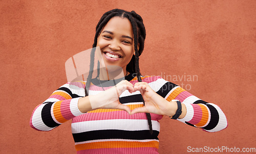 Image of Heart shape, portrait and black woman by a wall in the city while on a walk on a vacation. Happy, smile and beautiful African female with love hand gesture in a town while on holiday or weekend trip.