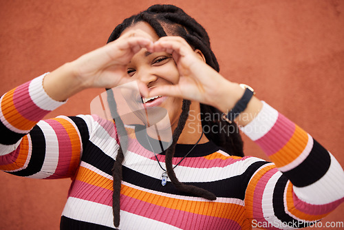 Image of Happy, heart shape and black woman by a wall in the city while on a walk on a weekend trip. Happiness, portrait and African female with a love emoji or hand gesture in town on holiday or vacation.