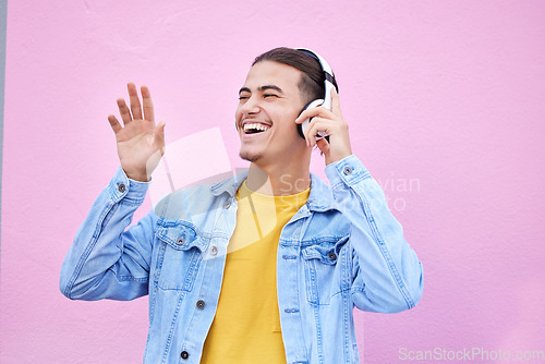 Image of Headphones, man and happy dance on pink background, wall backdrop or studio mockup. Excited guy listening to music, sound and streaming audio media with freedom, smile and hearing radio for dancing