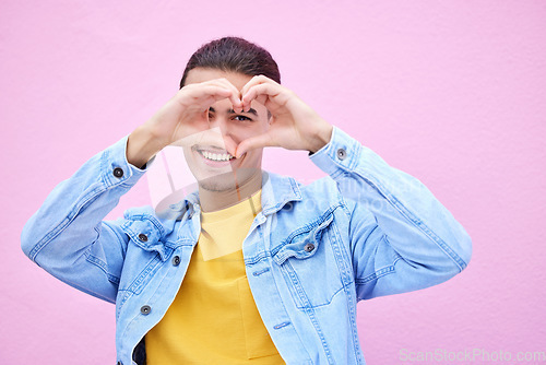 Image of Portrait, heart and valentines day with a man outdoor on a pink wall background for love or romance. Hand sign, romantic and gesture with a loving person showing affection against pastel color