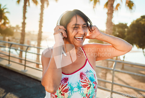 Image of Headphones, senior woman and laughing of a elderly person in Miami happy from summer holiday. Beach, music listening and web audio streaming of a old female with happiness on vacation in retirement