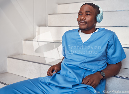 Image of Break, music and African doctor with headphones for a podcast, radio and audio on hospital stairs. Freedom, thinking and a male nurse listening to a track or songs while working in healthcare