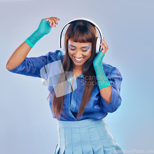 Image of Music headphones, dancing and woman with cyberpunk fashion and a smile on blue background in studio. Gen z model person with color clothes for dance while streaming and listening to futuristic audio