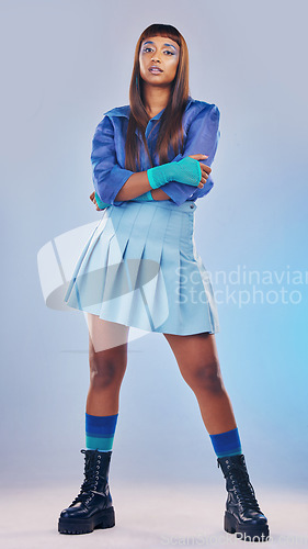 Image of Arms crossed, fashion and portrait of an edgy woman isolated on a blue studio background. Confident, cool and trendy model standing with fashionable clothes, stylish and elegant on a backdrop