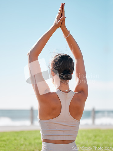 Image of Fitness, woman and yoga on grass by beach for spiritual wellness, exercise or meditation in nature. Sporty female yogi back in warm up arm stretch for zen workout, relax or meditating in the outdoors