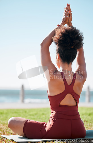 Image of Fitness, black woman and meditation on yoga mat by beach for spiritual wellness or exercise in nature. Sporty female yogi back in warm up arm stretch for zen workout, relax or awareness in meditating