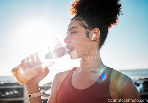 Image of Drinking water, fitness and black woman on beach exercise, listening to music and cardio training in blue sky lens flare. Liquid bottle for diet, goals and tired sports runner or USA person by ocean