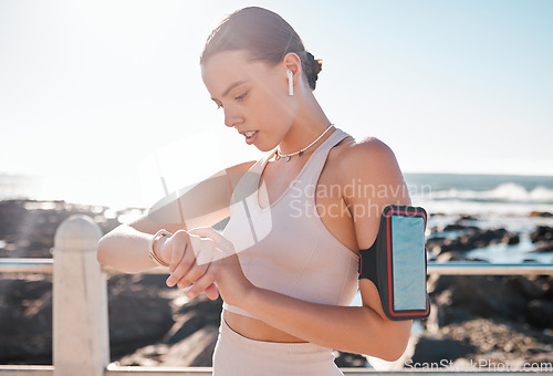 Image of Fitness time, smartwatch and woman with headphones checking running goals by the sea. Ocean, exercise app and workout timer with a runner by ocean water in summer after run and sports by a beach