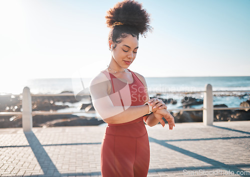 Image of Fitness, black woman and watch checking by beach for time, performance or tracking exercise in the outdoors. Happy African American female runner smiling looking at wristwatch for monitoring workout