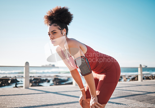 Image of Fitness, music and exhausted with a black woman runner on the promenade for cardio or endurance training. Exercise, running and earphones with a sports person feeling tired during her workout