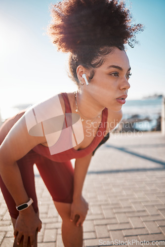 Image of Fitness, music and tired with a black woman runner on the promenade for cardio or endurance training. Exercise, running and earphones with a sports person feeling exhausted during her workout