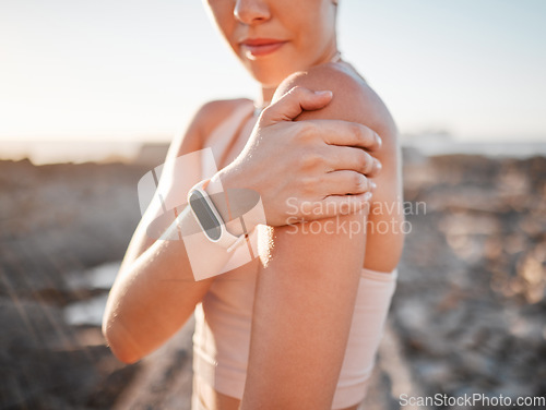 Image of Beach, fitness and woman with hand on shoulder pain standing on rocks at ocean. Nature, sports and injury during workout for health and wellness, muscle trauma during stretching exercise in morning.