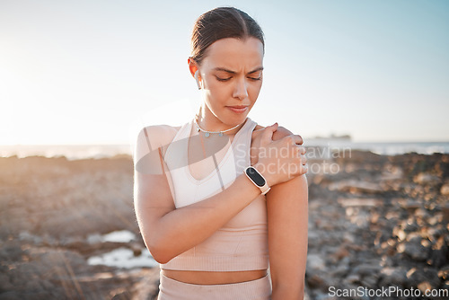 Image of Beach, fitness and yoga, woman with shoulder pain standing on rocks at ocean. Nature, sports and injury during workout for health and wellness, muscle trauma during stretching exercise in morning.
