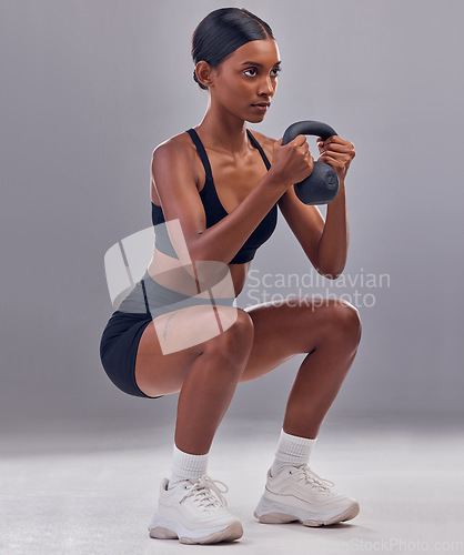 Image of Woman, kettlebell squats and exercise in studio for fitness, sports workout and focus wellness mindset. Strong female, bodybuilder or weights training for muscle power, energy or health on background