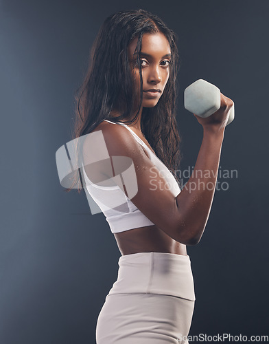 Image of Woman, portrait and bicep with dumbbell on black background, strong body and focus exercise. Indian female, bodybuilder and studio weights for fitness, power training and energy for sports workout